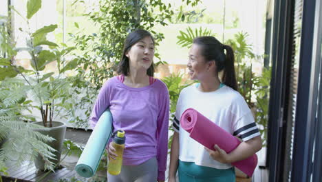 happy asian female friends with exercise mats walking and smiling on sunny terrace, slow motion