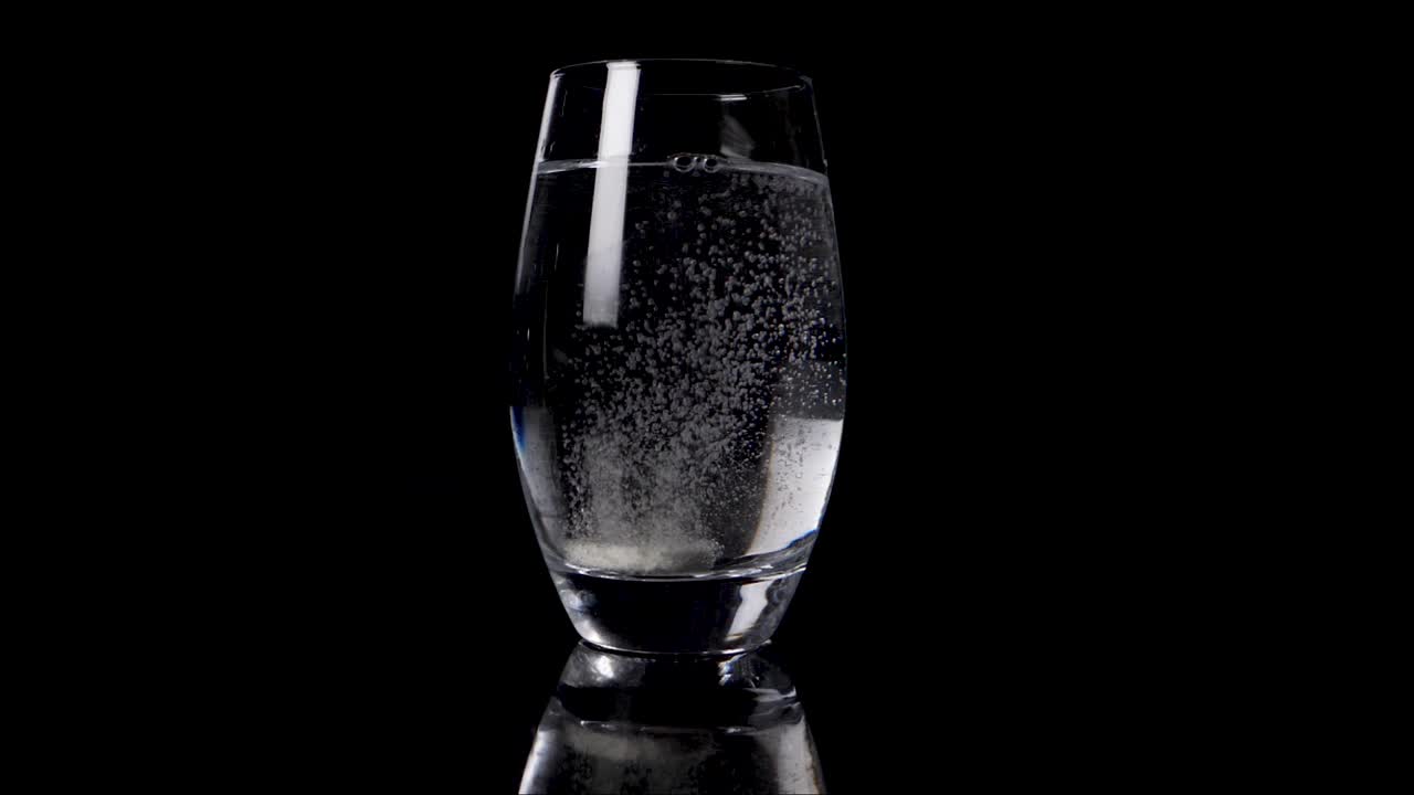 검은색 배경 앞에 깨한 물에 용해되는 비타민 알약이 떨어지는 느린 영상