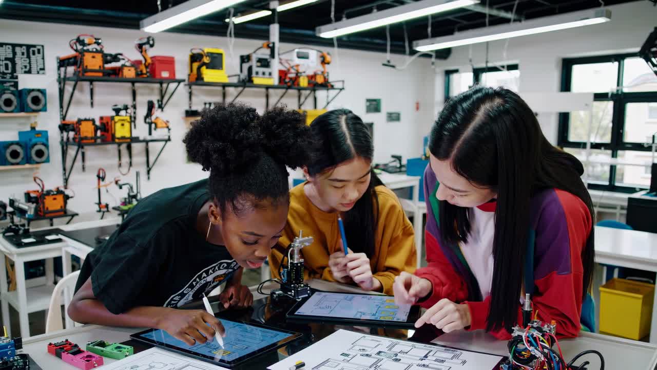 High-angle video of three diverse students collaborating on tablets in a tech lab