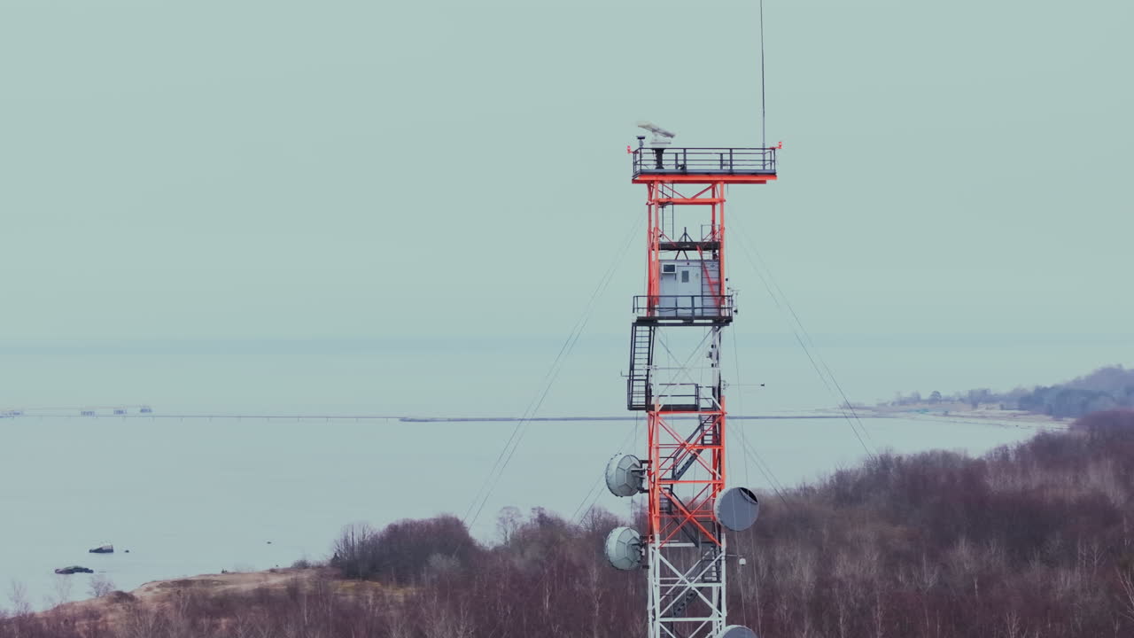 Aerial telephoto orbit of red and white radio tower at dusk with landscape in background, cable wires stretch and radar spins