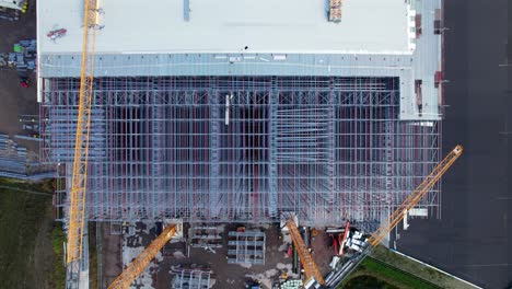descending drone shot of large steel building roof being built at construction site, aerial view