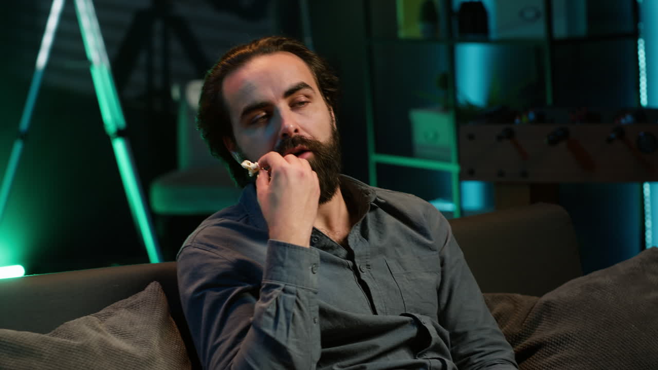 jugador aburrido jugando en la consola de televisión usando el gamepad, comiendo palomitas de maíz