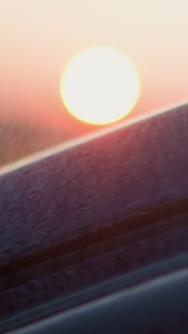 rain falls on car against dusk sun closeup. wet auto surface stands under rainstorm in evening countryside. romantic road trip on rainy season