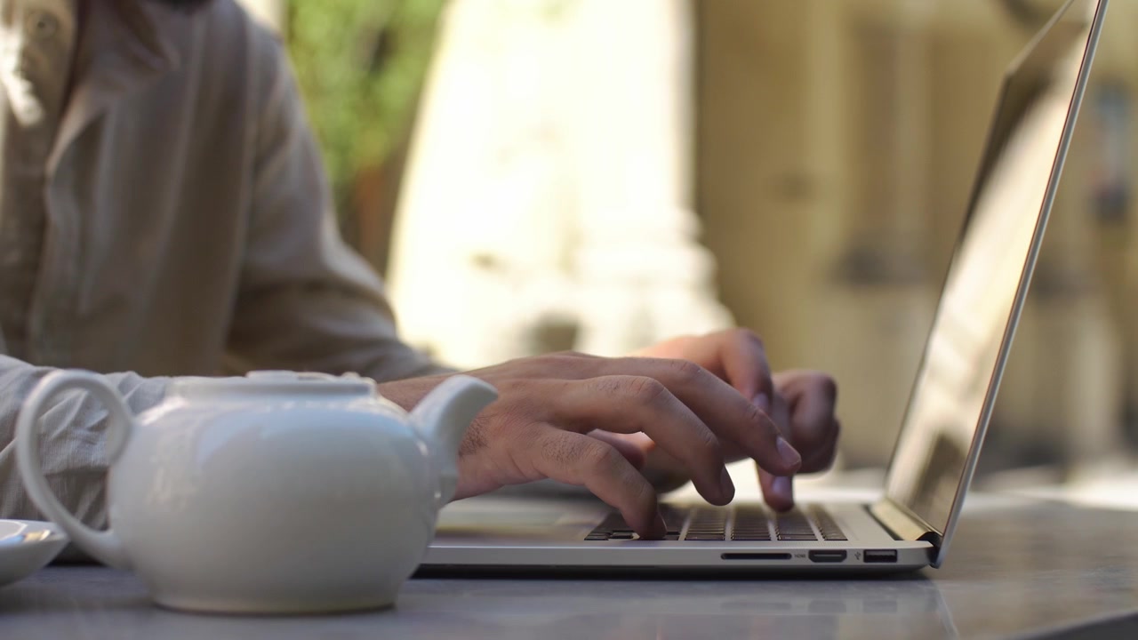 Persona che digita al laptop a un tavolo di un caffè all'aperto