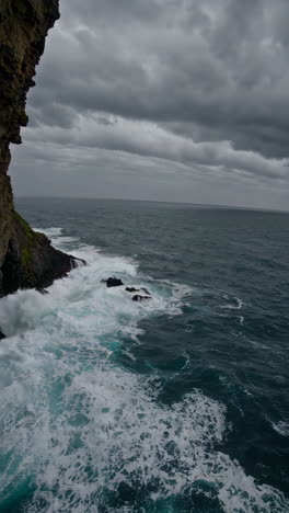 dramatic ocean waves crashing against cliffs under dark clouds