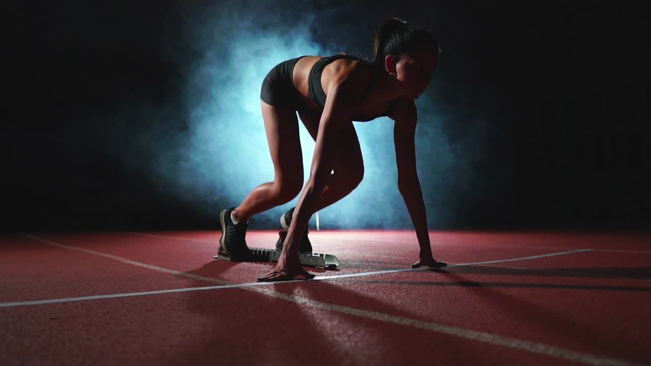 어두운 배경 에 있는 여자 운동 선수 는 어두운 배경 에 있는 트레드밀 에 있는 패드 에서 크로스 컨트리 스프린트 를 달리기 위해 준비 하고 있다