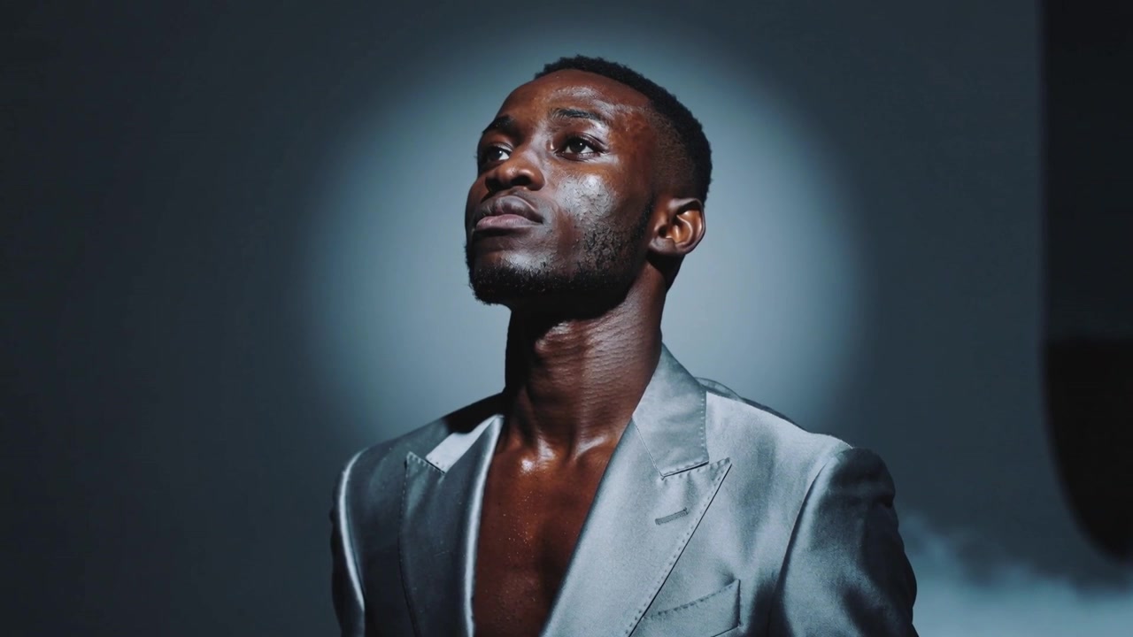 Lifting model tilting head upward in dark studio for fashion shoot, open silver blazer, halo fog