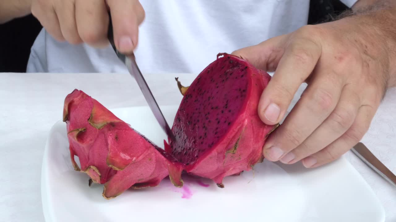 Person cutting a vibrant dragon fruit on a white plate
