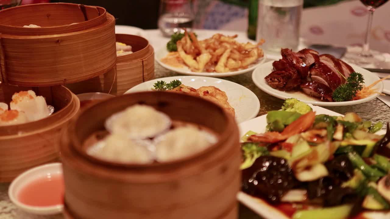 A variety of Chinese dishes on a glass table with a rotating lazy Susan, featuring dim sum and vibrant vegetables