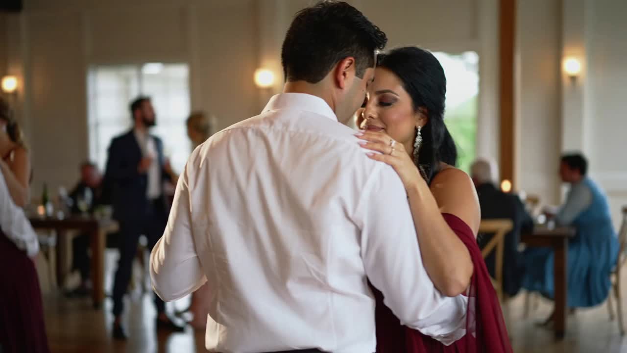 Wedding song starting, couple in white shirt and burgundy dress swaying at reception under lights