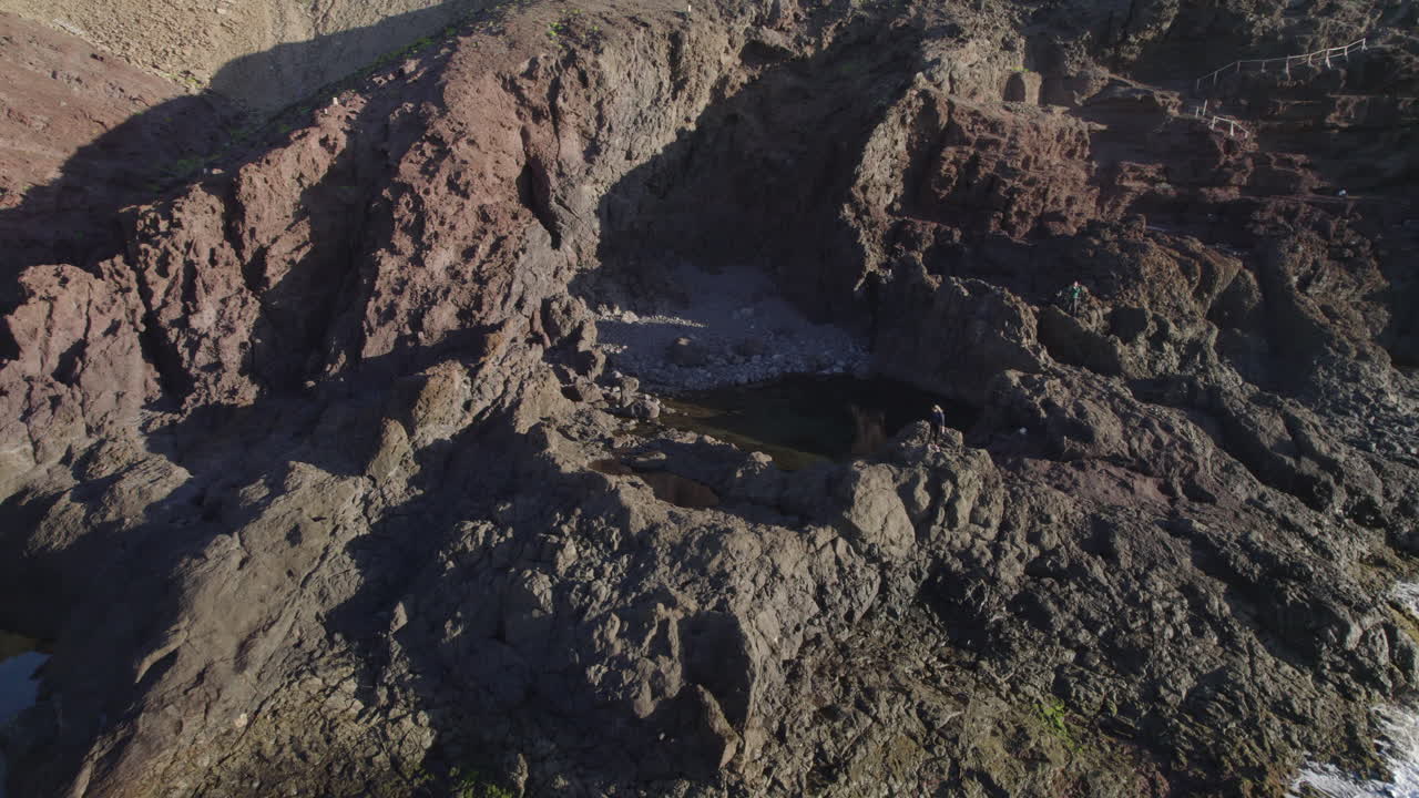 Luftfoto av turist som utforsker steinete kystlinje og naturlig basseng i Gran Canaria, Kanariøyene, Spania