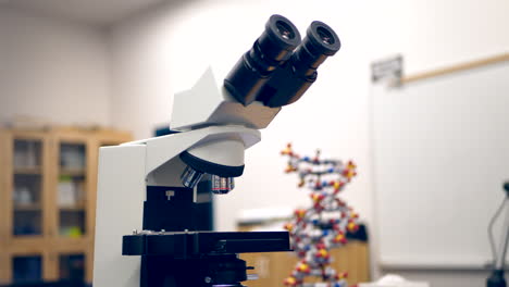 a microscope in a college biology research laboratory with a dna double helix educational figure and whiteboard in the classroom