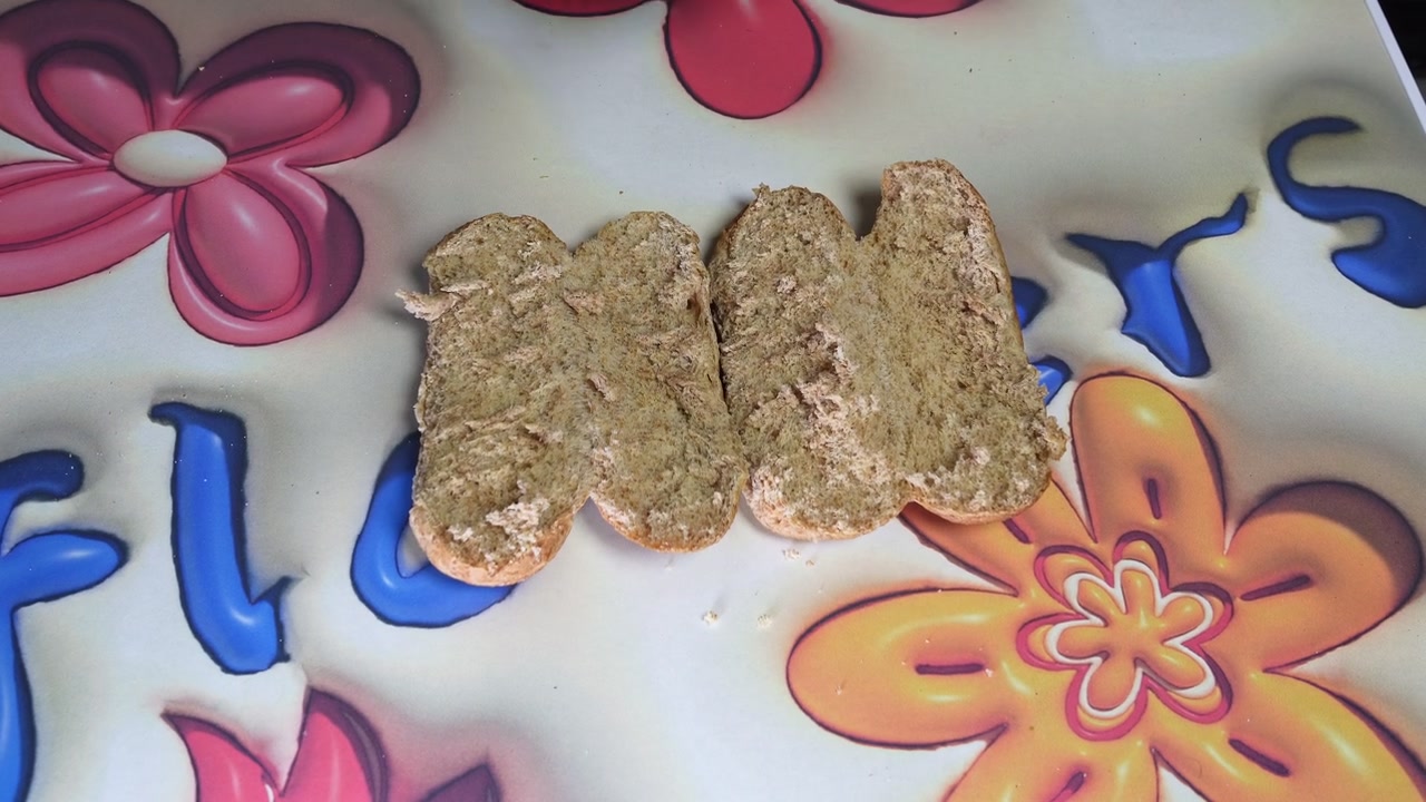 Top down close-up of male hands using a knife to prepare a brown bread sandwich on a colorful floral table. Making a healthy homemade snack indoors during daytime.