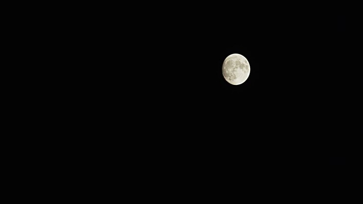 Tomada ampla em time-lapse de uma lua cheia enquanto ela sobe rapidamente do canto inferior esquerdo para o canto superior direito