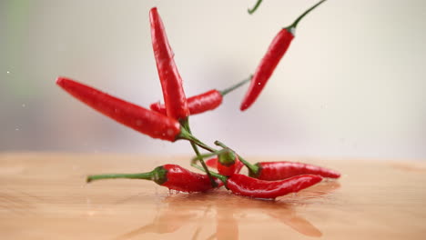 chili peppers falling onto the wooden kitchen table, bouncing and splashing water droplets around the kitchen in macro and slow motion