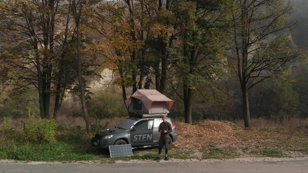 hombre joven frente a un camión todoterreno con carpa en la azotea y panel solar, estilo de vida nómada digital