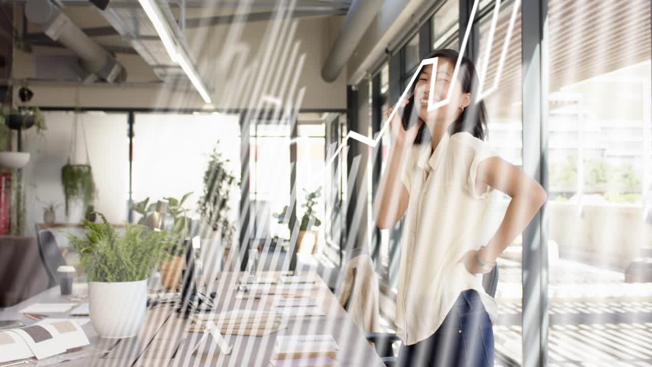 Businesswoman answering phone while reviewing laptop for work, animated line chart overlaying scene