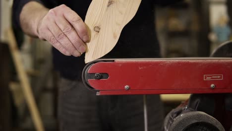 hombre muele el patrón de forma de pez con máquina de molienda con aserrín volando en los lados, profesión, concepto de carpintería. primer plano de hombre lijando madera en el taller. cámara lenta