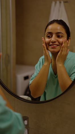 Happy-brunette-girl-with-Brown-skin-in-turquoise-pajamas-takes-care-of-her-body-skin-while-getting-ready-for-bed-in-the-evening-in-a-modern-apartment-in-front-of-a-mirror