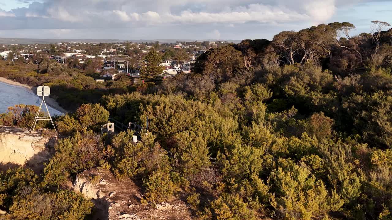 Drone glides above sandy cliffs, dense vegetation, and shoreline, revealing suburban Rye under golden sunlight