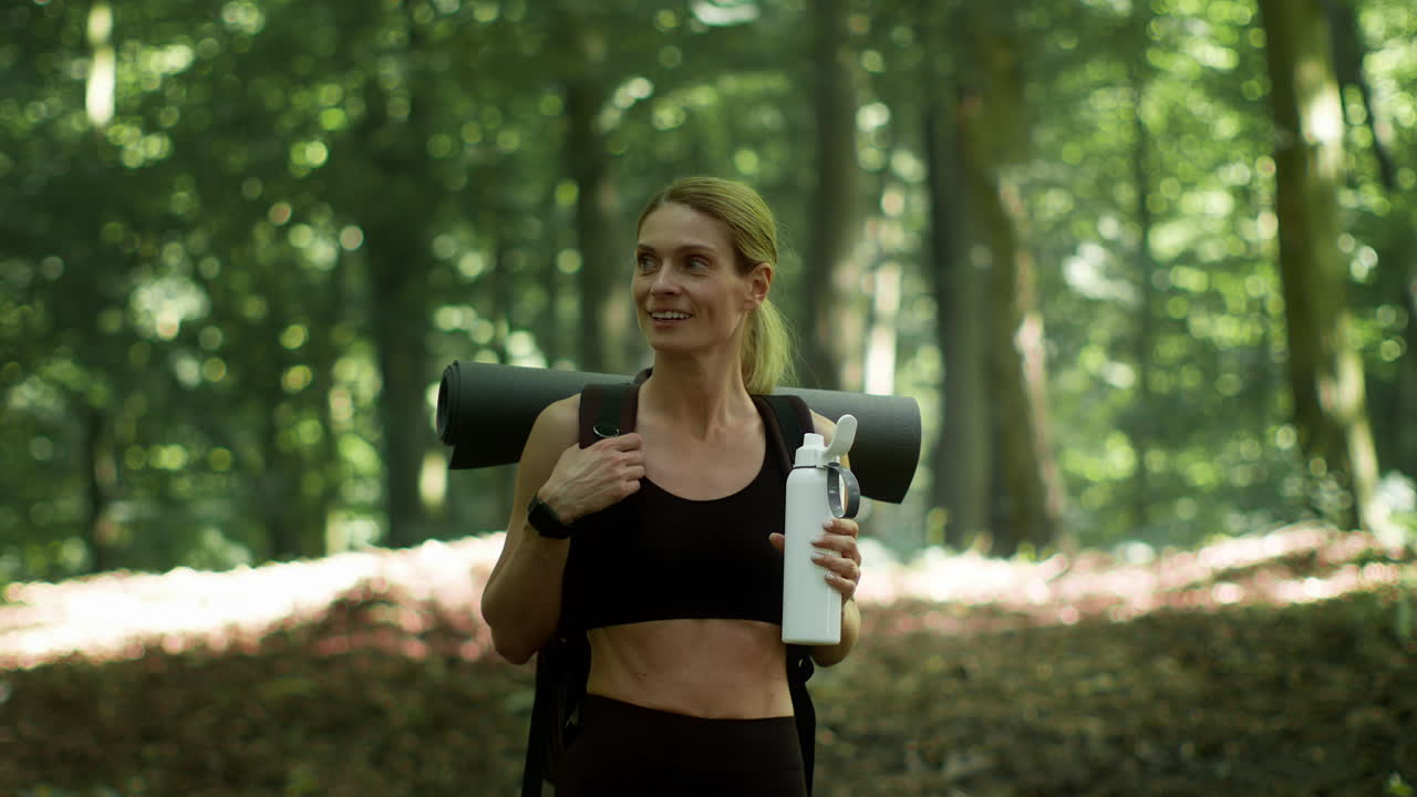 Woman with Yoga Mat and Water Bottle in Forest