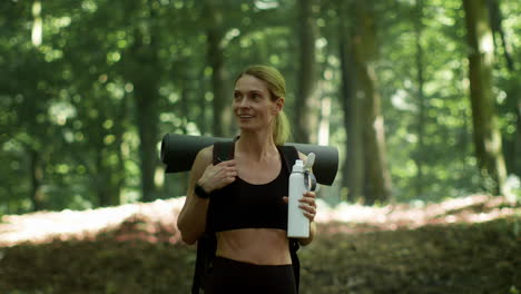 woman with yoga mat and water bottle in forest