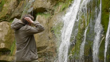 hiking on an overcast day - a young male hiker stops to admire the waterfalls and removes his hood - the route of the seven pools - catalonia spain - ruta dels set gorgs de campdevànol