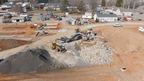 heavy machinery operates at a construction site, moving rocks and gravel. workers are busy sorting materials as the site is prepared for future development. dust and equipment fill the area.