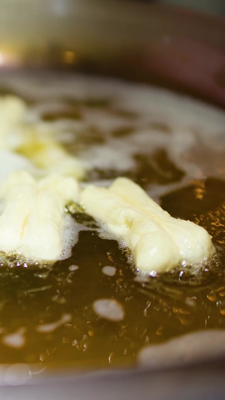 Close-up of traditional youtiao dough sticks frying in bubbling oil within a large metal wok.