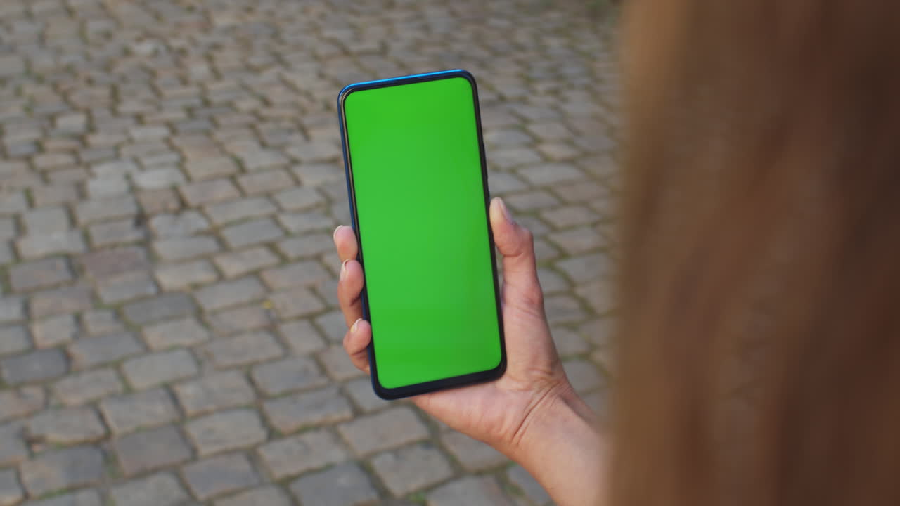 A person holds a smartphone with a green screen display outdoors