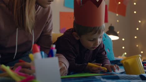 niño pequeño haciendo invitaciones para la fiesta de cumpleaños con la madre ayudando al hijo en el dormitorio colorido disfrutando de la imaginación creativa