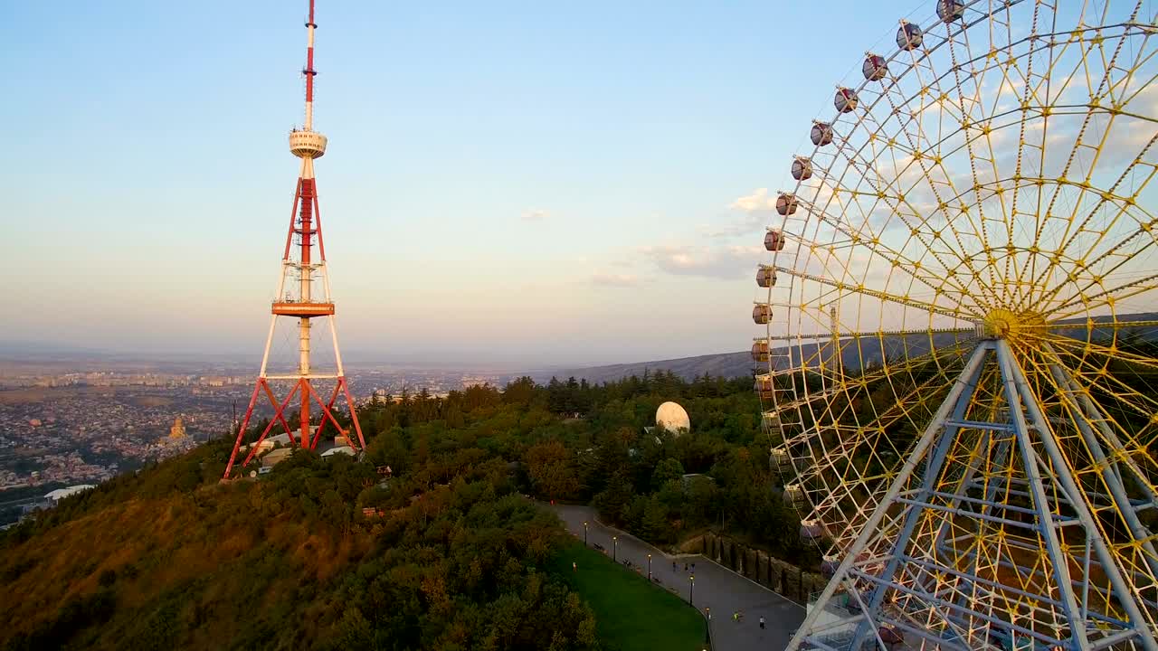 колесо обозрения и телевизионная башня на горе в солнечный день. редактирование видео с воздуха