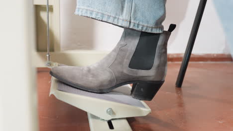 dress designer wearing black heel shoe keeps leg on industrial sewing machine pedal, adjusting pressure, ensuring smooth operation, focusing on garment production, demonstrating careful posture