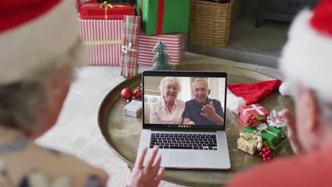 Pareja-Caucásica-Mayor-Usando-Una-Computadora-Portátil-Para-Una-Videollamada-Navideña-Con-Una-Pareja-Feliz-En-La-Pantalla