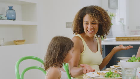 multi-racial family sitting around table in kitchen at home eating meal together