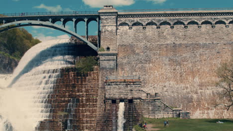 medium shot of new croton dam bridge and wall with stepped spillway, waterfall, and lawn visible with blue sky. slow motion 40 fps