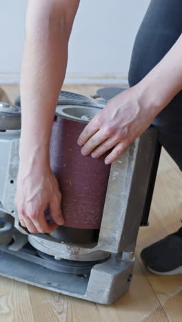 vertical close-up of sandpaper being changed on a floor sander used for pine wood floors.