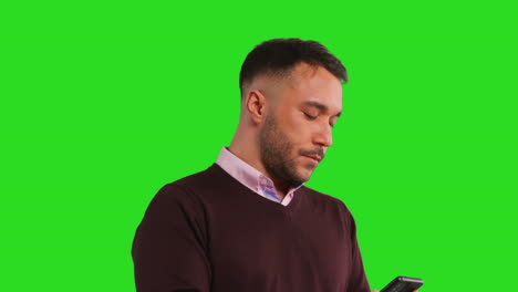 close up studio shot of businessman using mobile phone to message or browse online standing against green screen 1