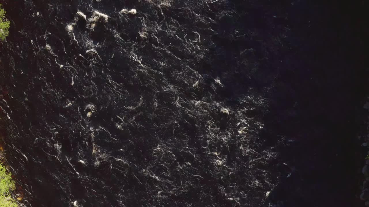 Downward view with the white foaming water of a dark colored mountain river