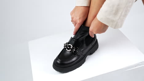 woman put one foot on the white cube to demonstrate stylish boot. lady touching the shoe with silver decorative chain. close up.