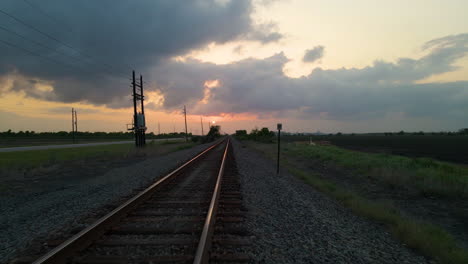 Drone-Shot-Following-Low-Over-Empty-Railroad-Tracks-Toward-Setting-Sun-In-Texas,-U