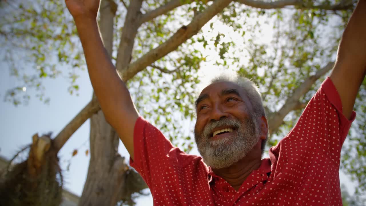 Low angle view of active African American senior man performing yoga in the garden of nursing home 4