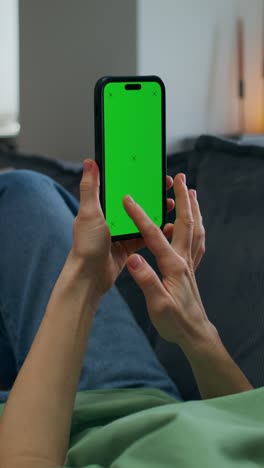 mujer usando un teléfono inteligente con pantalla verde en el sofá