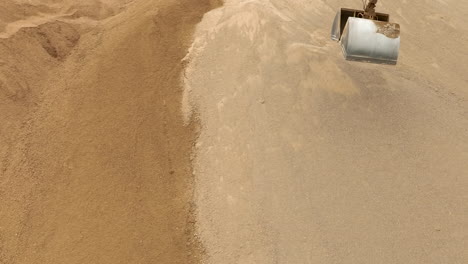 an aerial view of an excavator scoop digging into a sand pile, capturing the texture of the sand