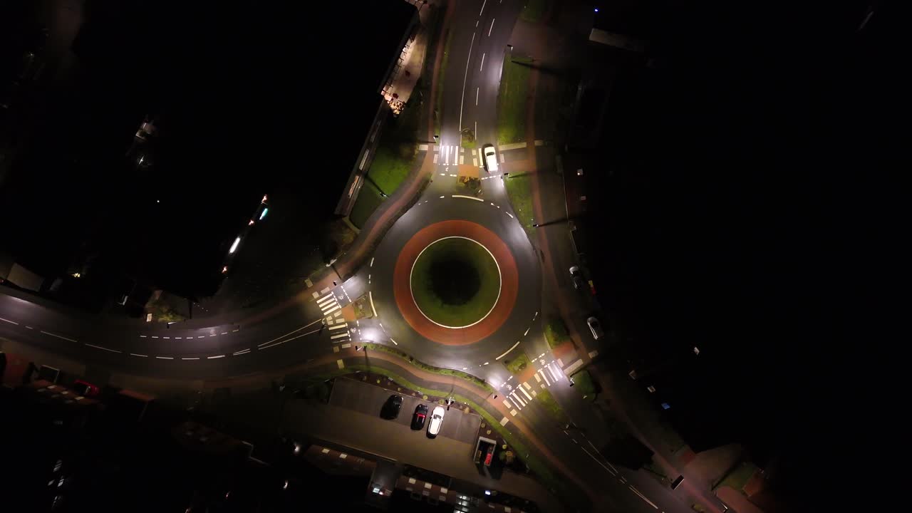 White car in illuminated roundabout at night. Small american town with glowing streetlights in quiet neighborhood. Aerial top down shot. Peaceful cityscape at midnight,USA.