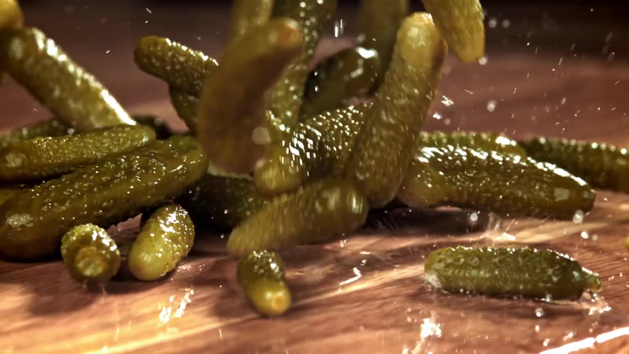 Cornichons tombant et éclaboussant sur une surface en bois au ralenti
