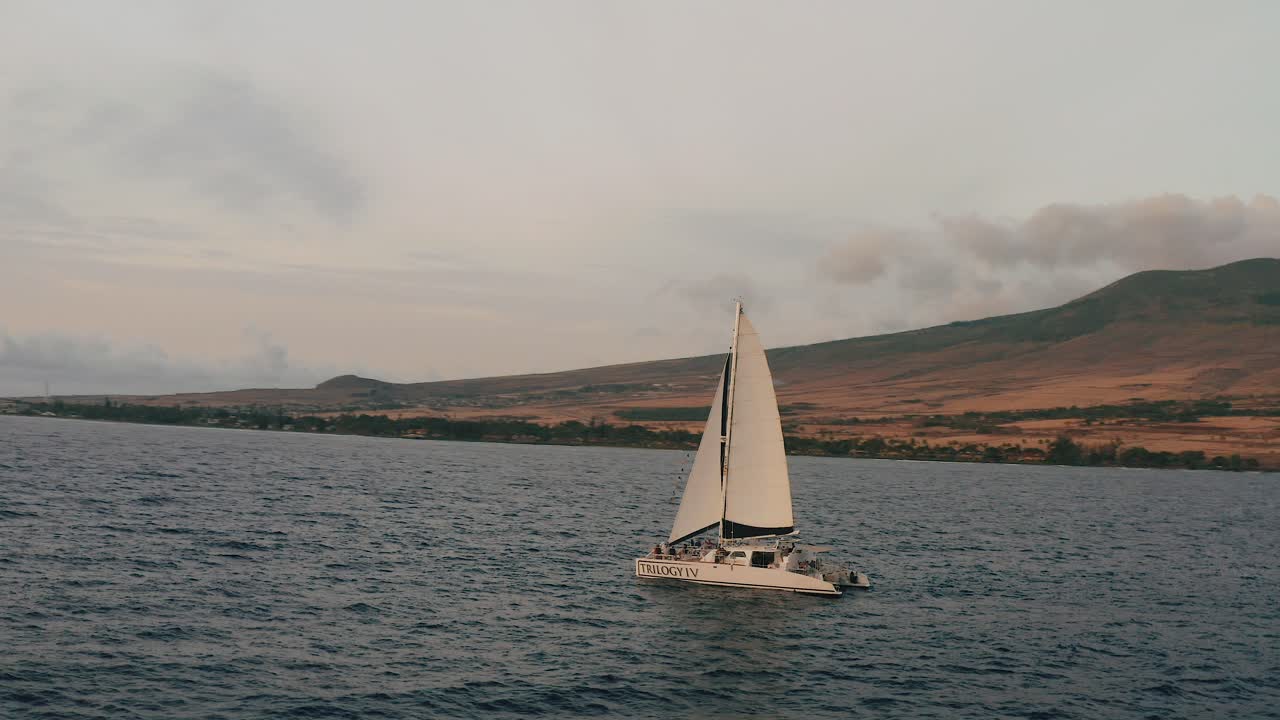 panorámica de drones aéreos de 4k sobre un velero que navega frente a la costa de hawaii al atardecer