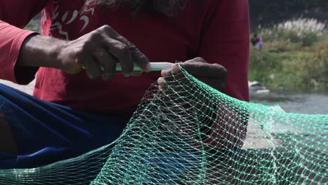 a south indian fisherman knitting a green nylon fishing net with basic hand tools