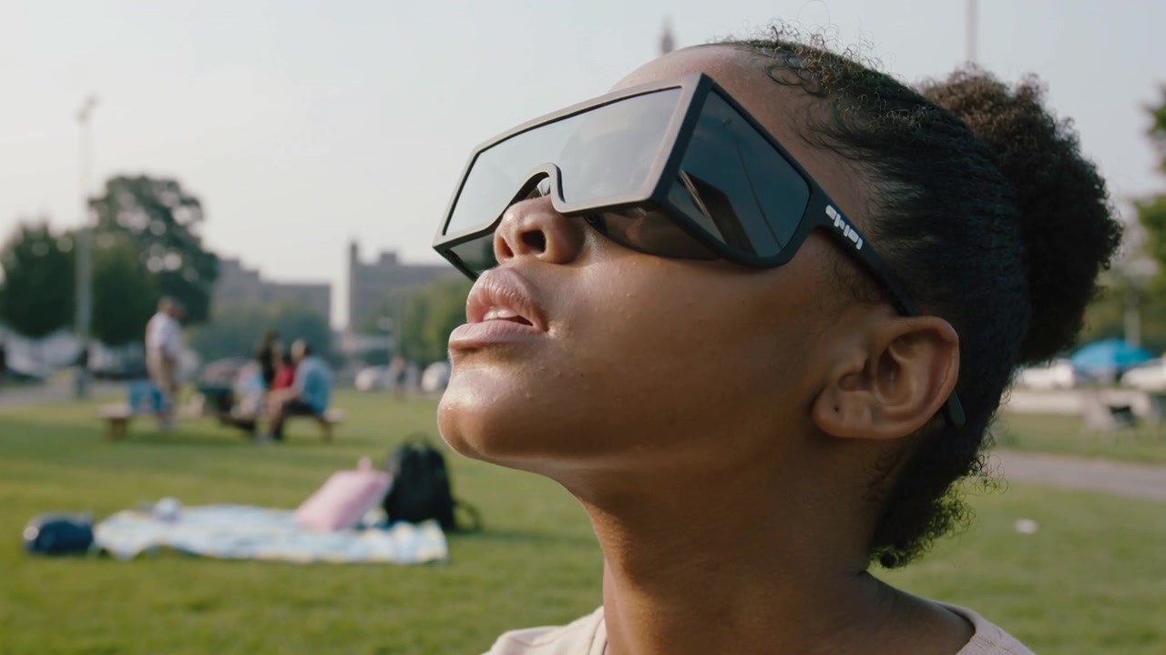 Spotting object above, teen girl wearing sunglasses, light top tilting chin tracking it in park