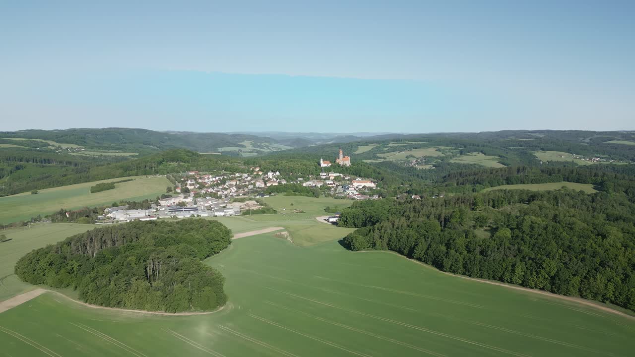 vista aérea del castillo de bouzov, en medio de campos verdes y densos bosques, con una pequeña ciudad cerca durante un soleado día de verano
